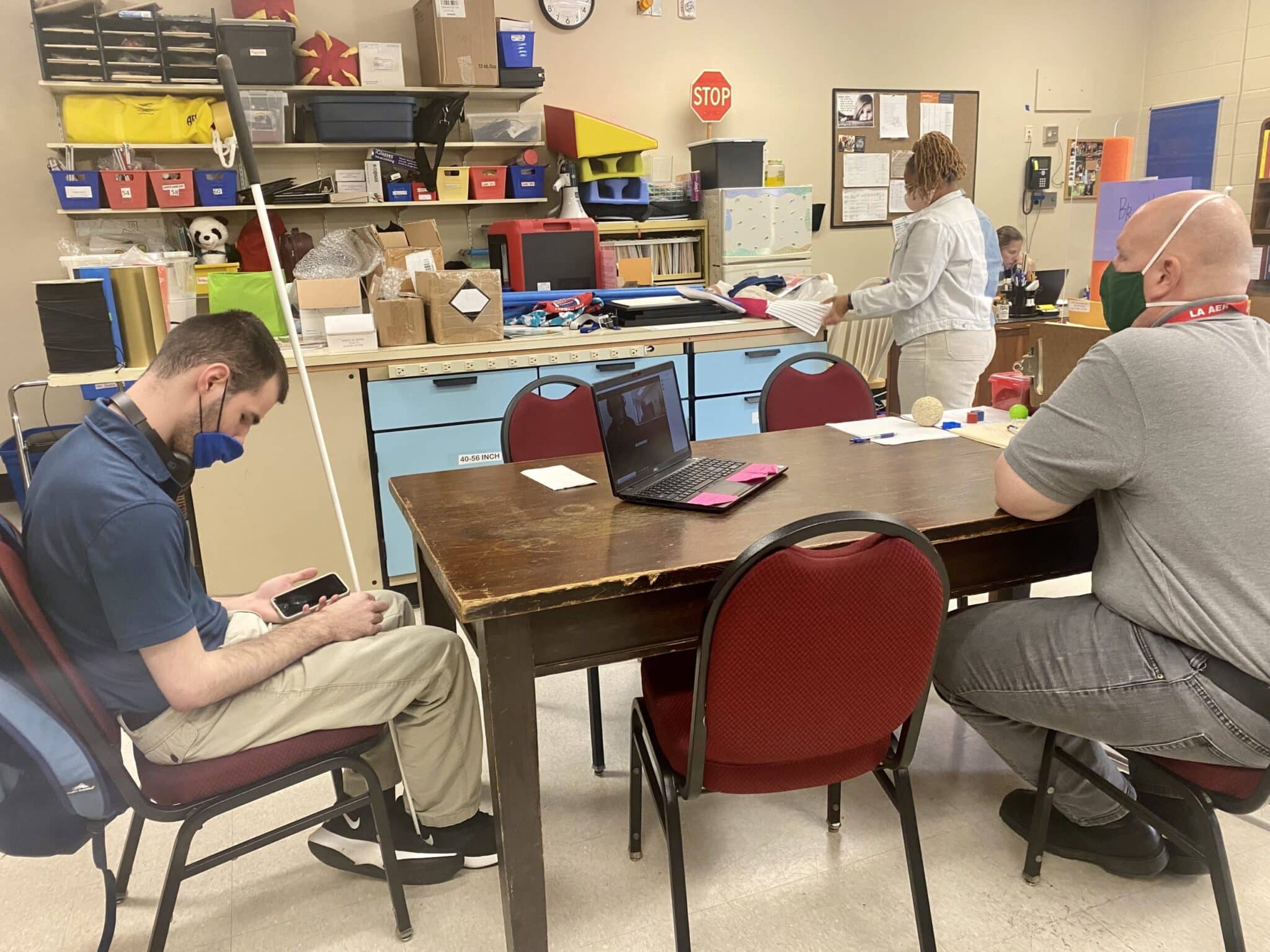 Kyle sits at a long table with an LSVI student using his iphone